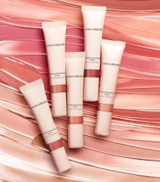 Five Laura Mercier tinted moisturizer blush tubes arranged over swatched peach and pink makeup textures.