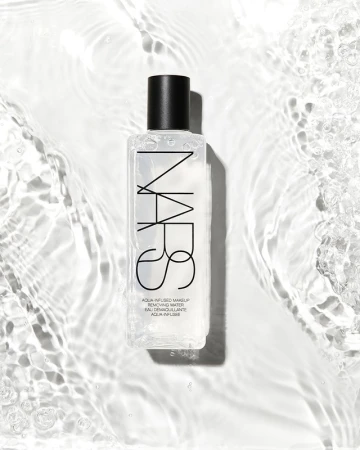 Overhead product shot of a clear rectangular NARS makeup removing water bottle resting in rippling water with bright lighting.