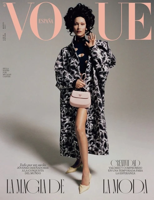 Vogue España cover featuring Bella Hadid in a black and white coat, holding a light pink Prada purse, and wearing nude heels against a gray backdrop.