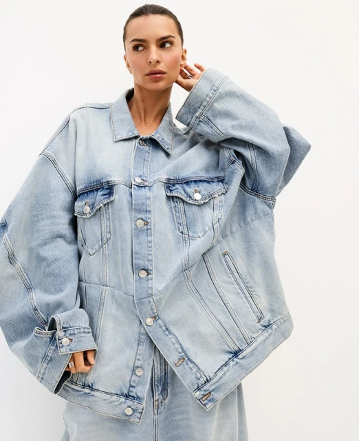 Adult woman wearing a light wash denim jacket and matching jeans against a neutral backdrop in a fashion studio setting.