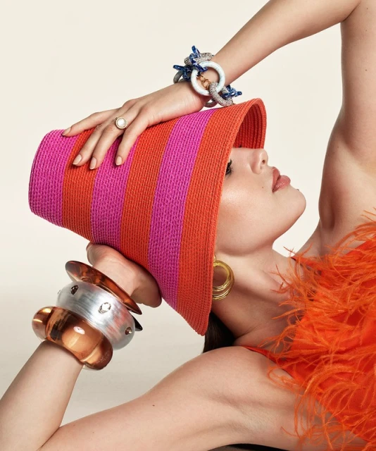 Woman poses with colorful hat and jewelry in a studio shot. The photo is an eye-level portrait with a neutral background.
