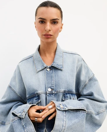 Close-up portrait of a woman wearing an oversized light blue denim jacket with stacked silver rings against a white seamless background