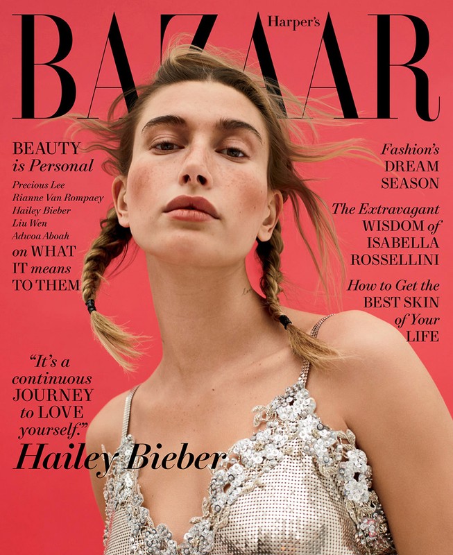 Magazine cover featuring Hailey Bieber in a silver beaded top against a coral pink backdrop with 'Harper's Bazaar' at the top.