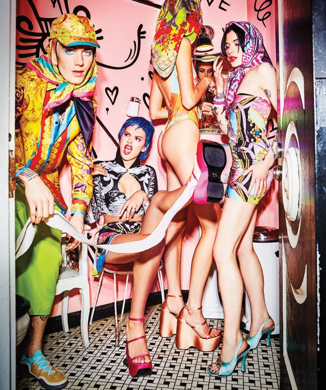 A group of five people wearing colorful patterned outfits in an indoor setting with tiled floor and pink walls, posing for a fashion shot.