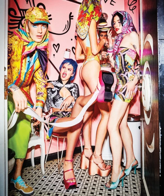 A group of five people wearing colorful patterned outfits in an indoor setting with tiled floor and pink walls, posing for a fashion shot.