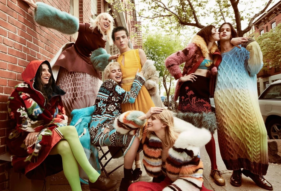 Group of young people in colorful outerwear posing outdoors, brick building background, fashion editorial style, diverse, vibrant clothing.