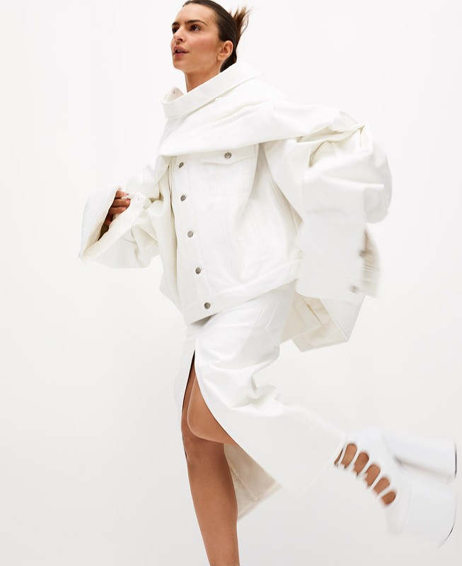 A woman in motion poses in an all-white ensemble consisting of a jacket, skirt, and shoes against a bright white backdrop.