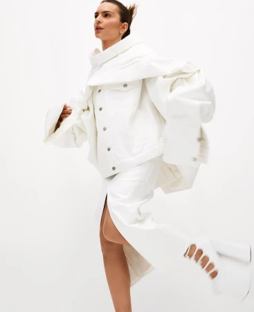 A woman in motion poses in an all-white ensemble consisting of a jacket, skirt, and shoes against a bright white backdrop.
