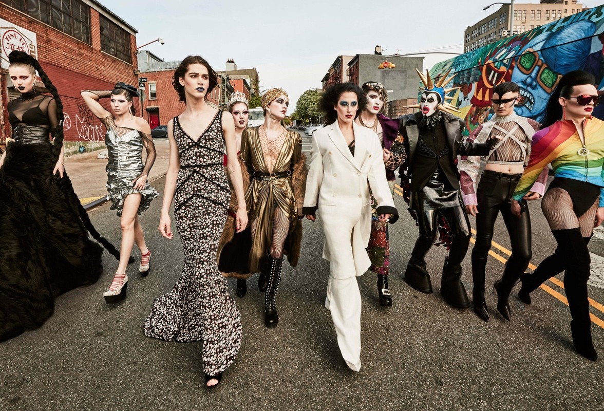 Group of diverse people in fashionable outfits walking on city street with colorful graffiti art, brick buildings, and asphalt road.