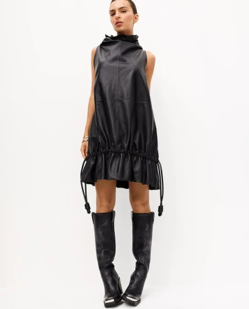 Model in a black leather mini dress and black leather boots standing against a white seamless background