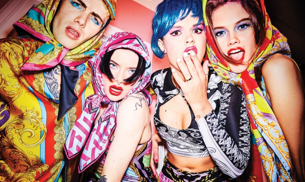 Four people wearing patterned headscarves and outfits with vibrant makeup. Fashion shot for editorial or commercial use.
