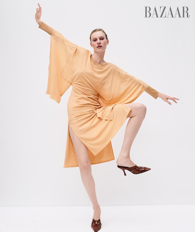 Fashionable woman in a peach-colored dress poses dynamically against a white background, showcasing modern style and editorial flair.