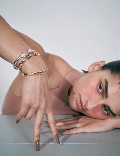 Woman poses with stylish gold and silver bangle bracelets featuring animal head designs in a minimalist studio setting.