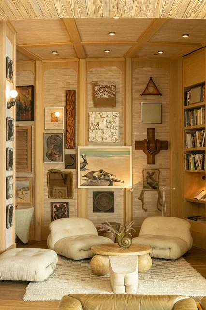 Living room interior with two white armchairs, a round coffee table with a conch shell, and a gallery wall featuring a diverse art collection.