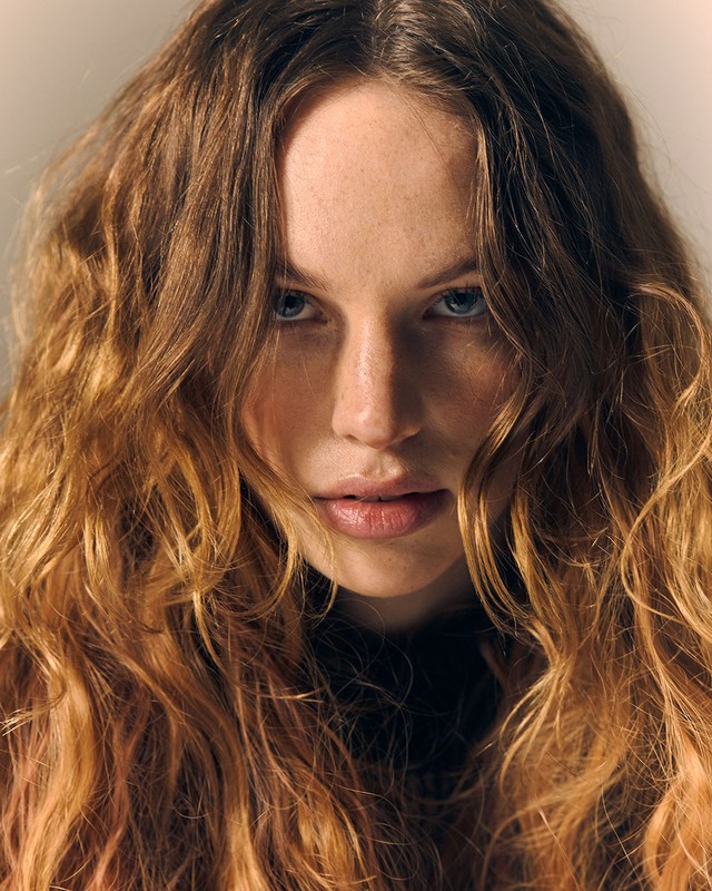 Portrait of a red-haired woman with blue eyes, captured in soft studio lighting, highlighting her wavy hair and natural complexion.