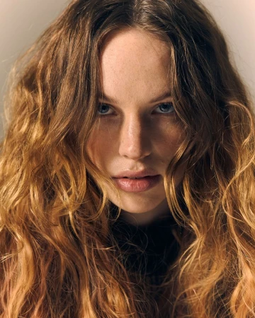 Close-up portrait of a woman with long wavy blonde hair and blue eyes looking directly at the camera.