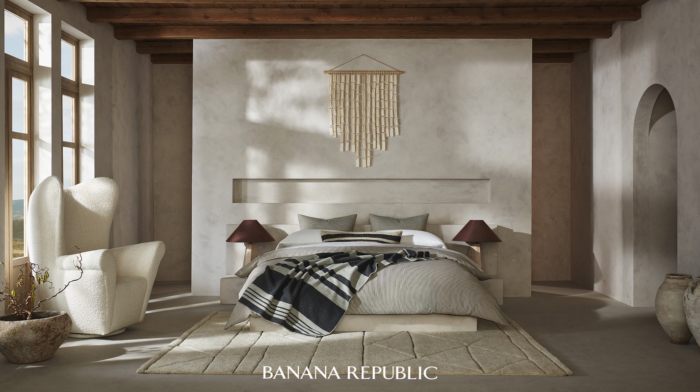 Bedroom interior showcasing a made bed, accent wall, bamboo wall hanging, modern lighting, rug, armchair, and large windows.