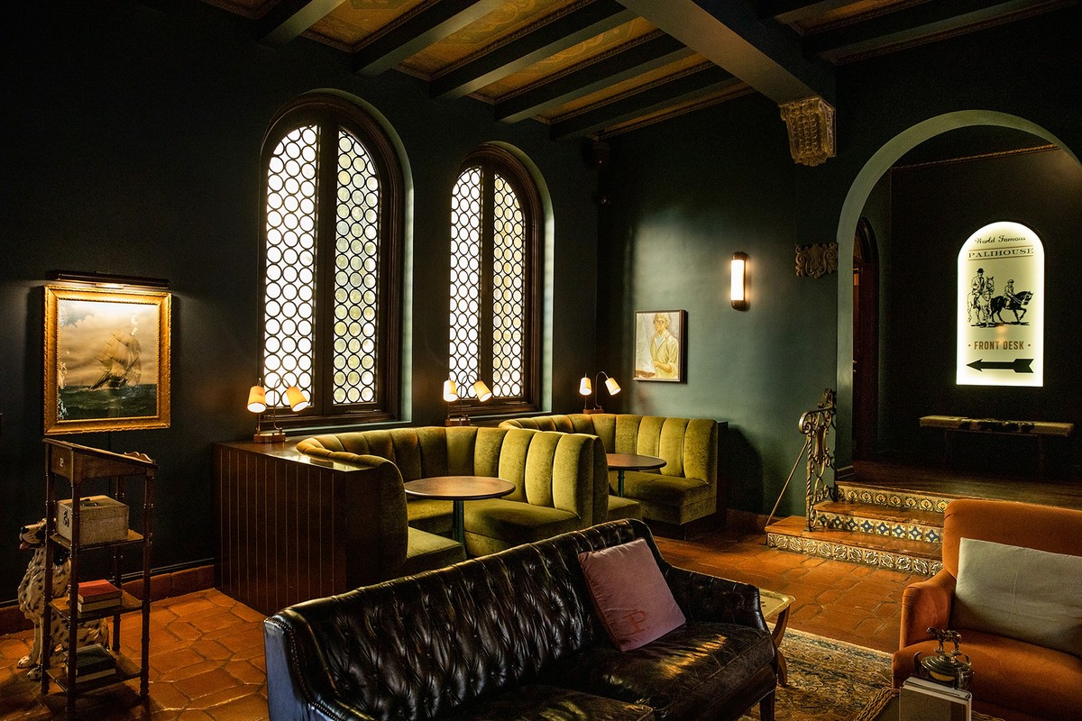 Interior view of an upscale lounge with olive-green booth seating, dark-green walls, leather furniture, and large arched windows.