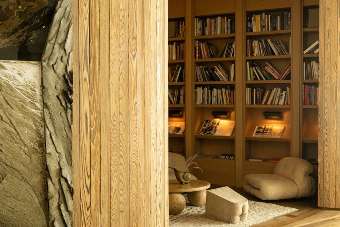 Reading nook with a bookcase and comfortable seating in a warm, inviting space with textured walls and a unique wooden post.