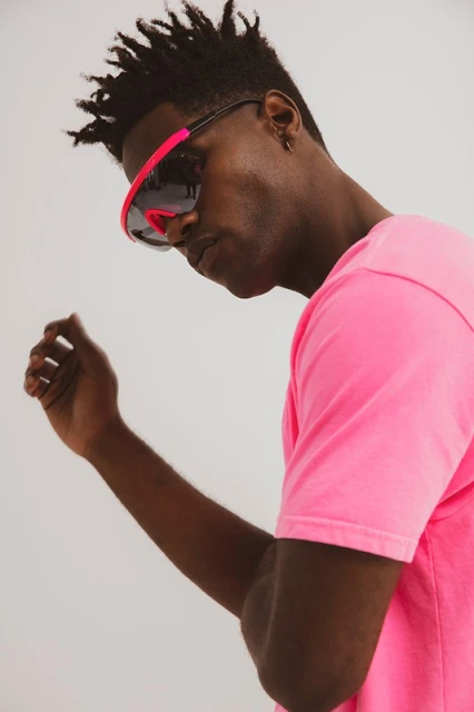 Portrait of a Black male in a hot pink shirt and futuristic sunglasses against a neutral background. Fashion, style, and portraiture.