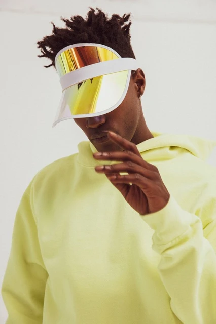 Person wearing a bright-yellow hooded sweatshirt and a reflective visor, against a white background, in a studio shot.