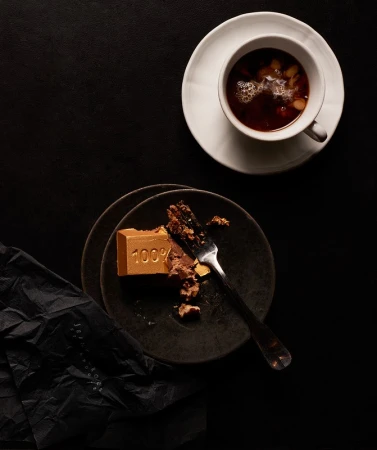 Overhead shot of chocolate cake, dessert fork, and hot beverage on a dark background, showcasing dark-tone food photography.