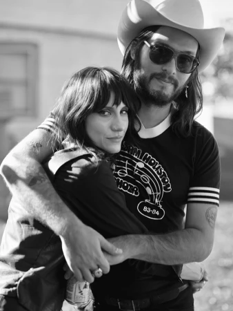 Black and white portrait of a man wearing a cowboy hat and sunglasses hugging a woman with dark hair in Los Angeles.