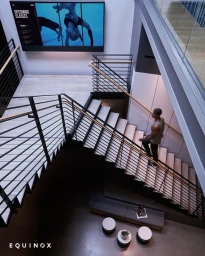 High angle shot of a person walking up modern interior stairs with dark metal railings and light wood steps.