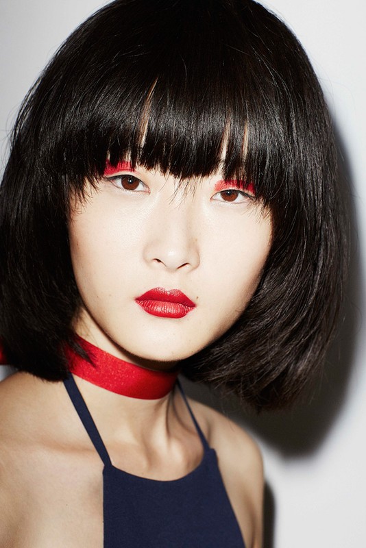 Close-up portrait of an Asian female model with black hair, red lipstick, and red eyeliner. She is wearing a navy blue top.