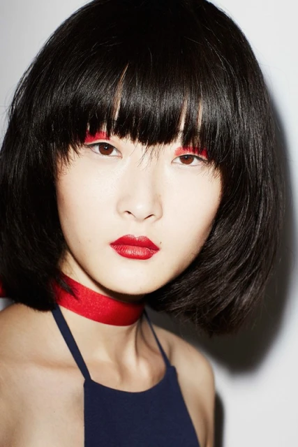 Close-up portrait of an Asian female model with black hair, red lipstick, and red eyeliner. She is wearing a navy blue top.