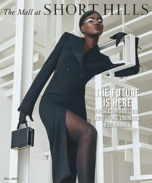 Fashion magazine cover featuring a Black female model in a black dress with a slit, black tights, gloves, and a black purse.