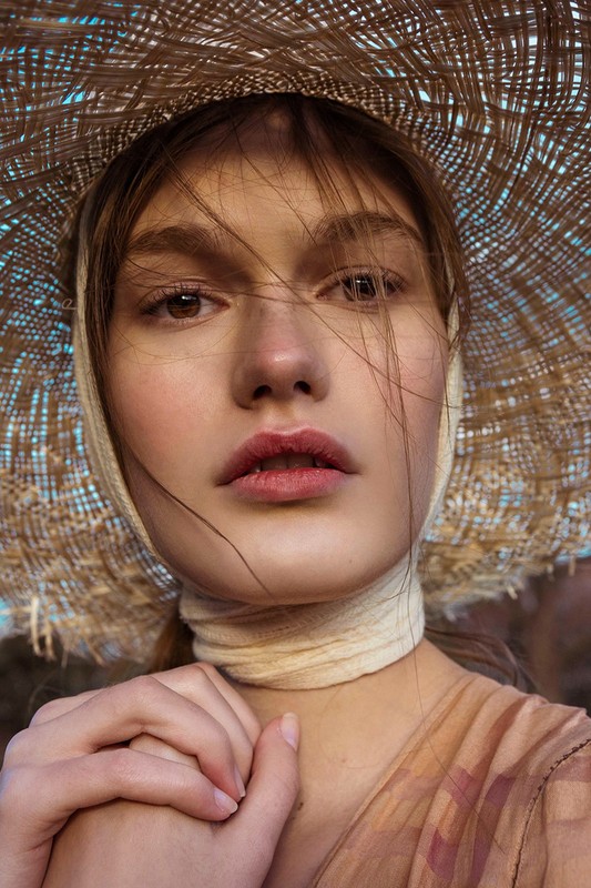 Close-up portrait of a woman wearing a wide-brimmed straw hat and a wrapped scarf, styled with makeup by Misuzu Miyake.
