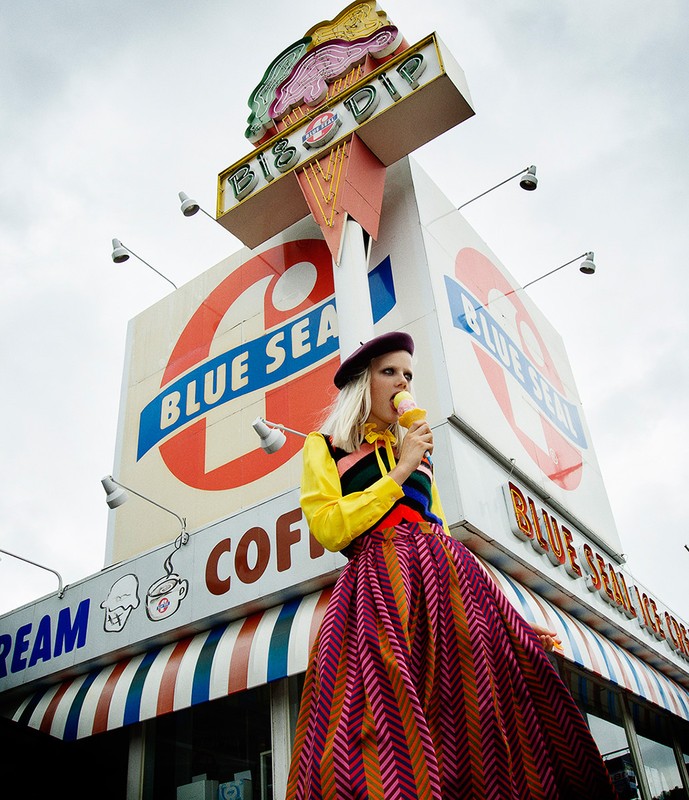 A fashionably dressed woman enjoys ice cream in front of the Blue Sea BisB Dip shop featuring a vintage awning and outdoor lighting.