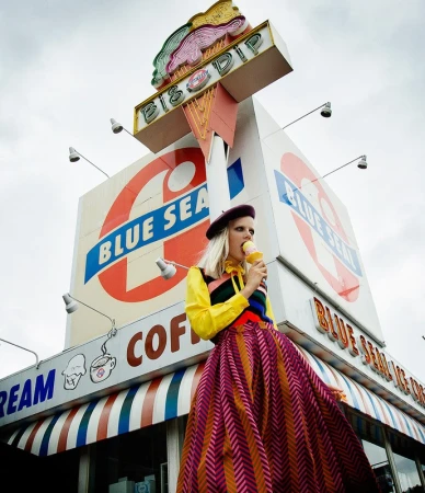A fashionably dressed woman enjoys ice cream in front of the Blue Sea BisB Dip shop featuring a vintage awning and outdoor lighting.