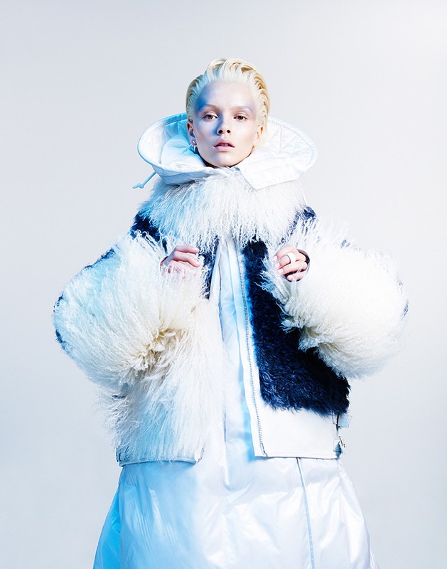 Woman in a unique high-fashion outfit with an ornate collar and fluffy jacket, gazing directly at the camera in a studio setting.