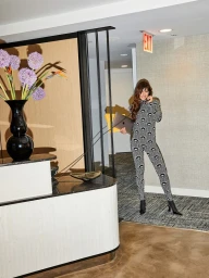 Woman in patterned jumpsuit holding a laptop and landline phone in an office lobby with floral arrangement