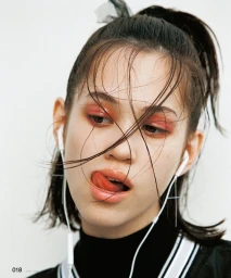 Close-up portrait of young woman with pink eyeshadow, high ponytail, and white wired earphones against a plain white background