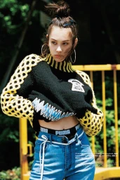 A young woman with a top-knot bun wearing a black and yellow knit sweater and blue jeans outdoors