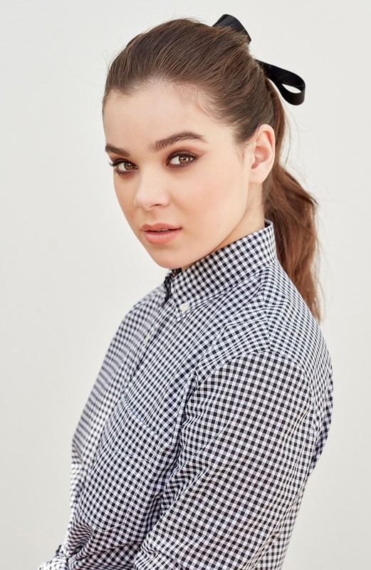 Young woman in a gingham shirt with a black ribbon in her hair poses in a close-up studio shot on a plain background.