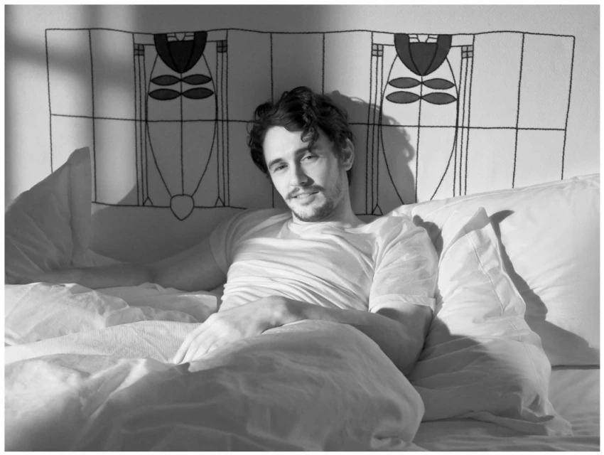 Monochrome portrait of a man lying in bed with a decorative headboard, captured in a soft, diffused light, emphasizing a serene and relaxed mood.