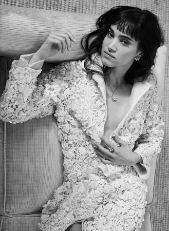 Black and white portrait of a woman wearing an intricate floral lace jacket reclining on a textured sofa by Mona Kuhn.