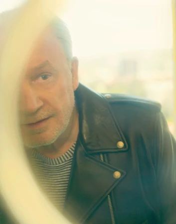 Portrait of an older man wearing a black leather jacket and striped shirt shot through a partially obscured lens.