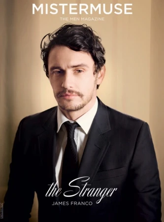 Portrait of actor James Franco wearing a black suit and dark tie against a plain neutral background.