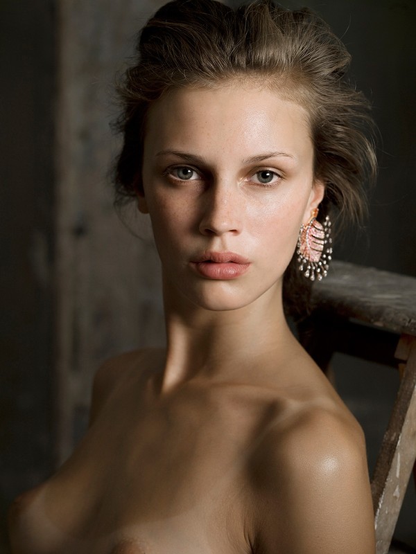 Portrait of a bare-chested young woman with pink earrings against a neutral background, natural light. Beauty and fashion concept.