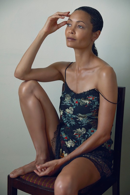 Elegant portrait of an adult woman with her hand to her forehead, wearing a floral camisole and seated on a vintage wooden chair.