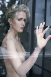 Portrait of Sarah Paulson looking back over her shoulder with her hand pressed against a glass window