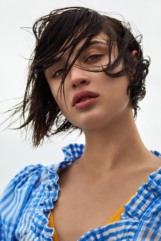 Portrait of a brunette adult woman with wet hair, wearing a blue and white checkered top, looking directly at the camera.