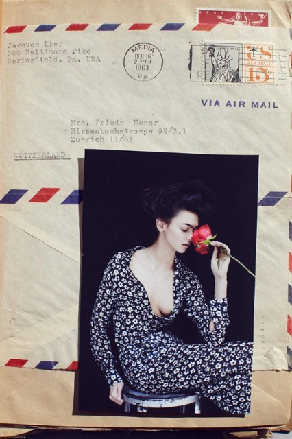 Fashion photo of a woman smelling a red rose, seated on stool, set against vintage envelopes with postage stamps and airmail markings.
