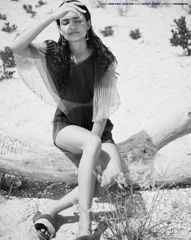 Editorial shot of a woman in a dress sitting on a log with her hand shielding her eyes, in a desert-like setting in black and white.