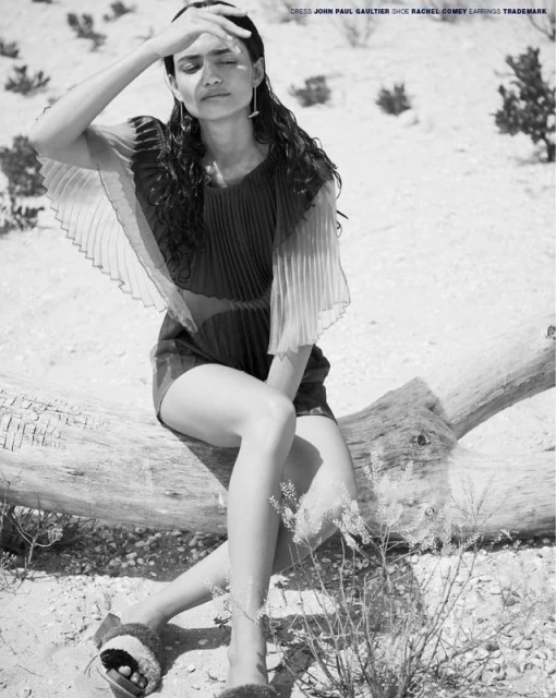 Editorial shot of a woman in a dress sitting on a log with her hand shielding her eyes, in a desert-like setting in black and white.